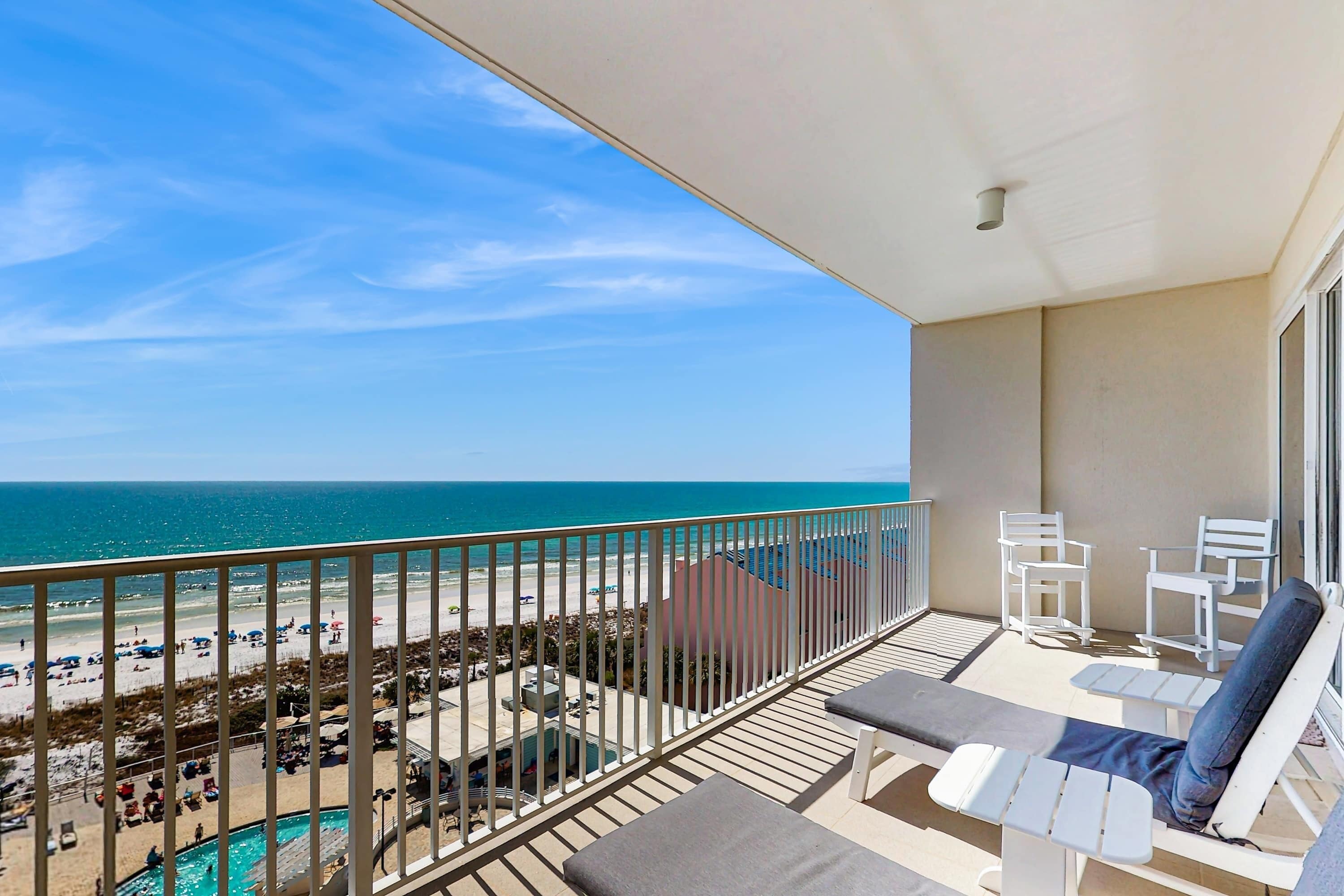 A balcony with a view of the beach and ocean. There are lounge chairs and a pool area visible.