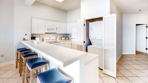A modern kitchen with white cabinetry, a central island with bar stools, and a built-in microwave. - 2BR Gulf-front condo with ocean views (Miramar Beach)