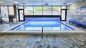 Una piscina interior con paredes de vidrio transparente, suelo de piedra y un banco a un lado.