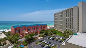 Um hotel com estacionamento, uma praia e um edifício grande com telhado azul.