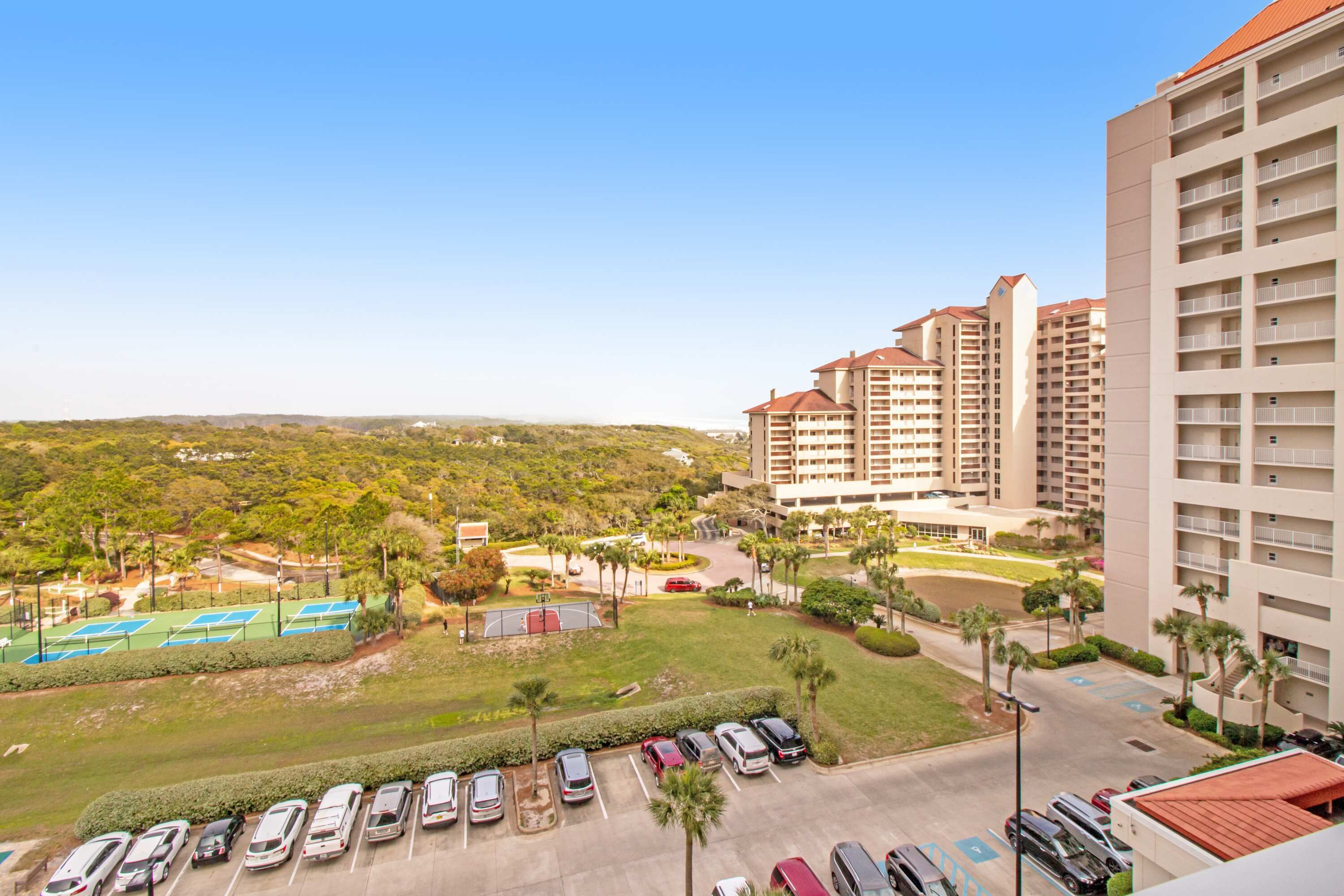 Un hôtel de grande hauteur doté de nombreux balcons, d’un parking et d’un court de tennis.