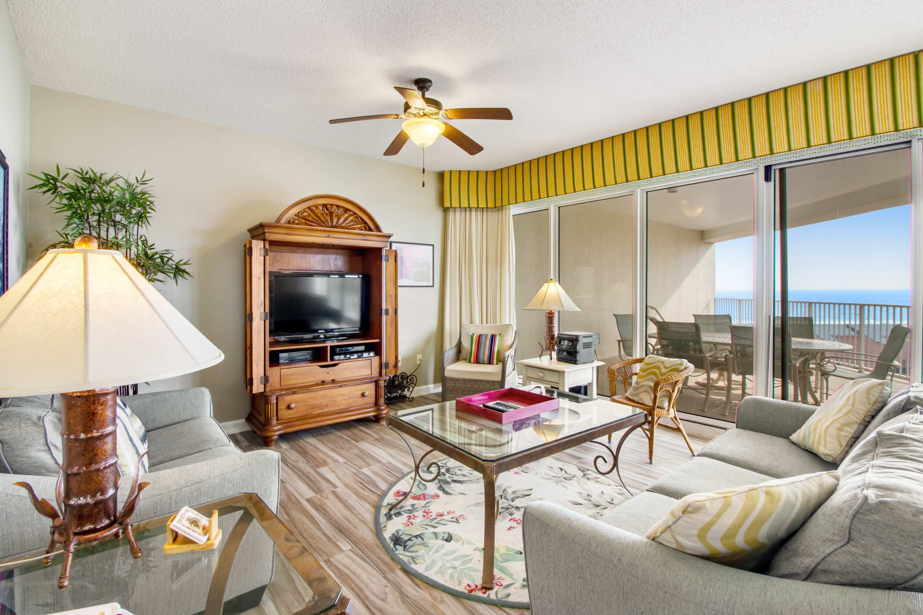 A living room with a television, sofa, and chairs, a glass coffee table, and a ceiling fan.