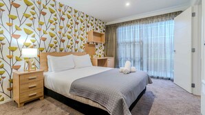 Una camera da letto ordinata con un letto grande, un comodino con una lampada, una mensola a parete e una finestra con tende.