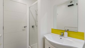 Un bagno moderno con box doccia in vetro, un lavandino bianco con schienale giallo e uno specchio grande sopra il lavandino.