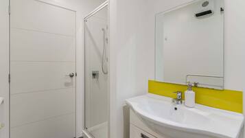 A modern bathroom with a glass shower enclosure, a white sink with a yellow accent backsplash, and a large mirror above the sink.