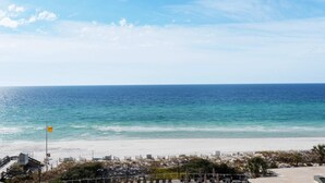 A beach view with a clear sky, a flag, and a sandy area with structures. - Exclusive 2BR beachfront condo with gulf views (Miramar Beach)