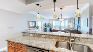 A modern kitchen with granite countertops, stainless steel sink, wooden cabinets, and pendant lighting. - Exclusive 2BR beachfront condo with gulf views (Miramar Beach)