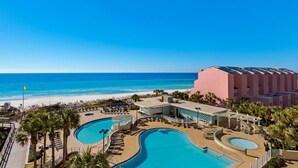 Un resort con una gran piscina, una playa y un edificio rosado.