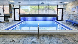 An indoor swimming pool with stone flooring, a blue tiled border, and a bench along the wall. - Beachfront condo with Gulf views (Miramar Beach)