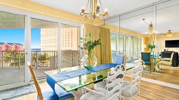 A modern dining area with a glass table, white chairs, and a view of the cityscape through large windows. - Beachfront condo with Gulf views (Miramar Beach)
