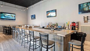 A bar area with a long counter, multiple bar stools, and a television mounted on the wall displaying sports. - 2BR Beachfront, Gulf Views, Sleeps 6 (Miramar Beach)