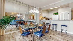 A spacious dining area with a glass table and metal chairs, a kitchen with white cabinets, and a large mirror reflecting the room. - Exclusive Gulf-Front Condo with Balcony (Miramar Beach)