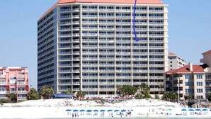 Ein mehrstöckiges Hotel mit rotem Dach in der Nähe eines Strandes mit weißem Sand und blauem Wasser.