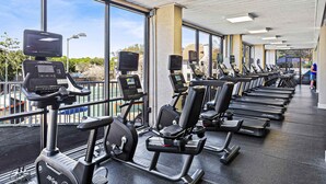 Ein Fitnessstudio mit Reihen von Ergometer- und Laufbändern, großen Fenstern und freiem Blick nach außen.