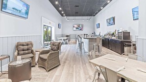 Un vestíbulo de hotel moderno con mobiliario de mimbre, una zona de bar y varias pantallas mostrando contenido.