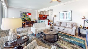 A modern living room with a sofa, armchair, coffee table, and a lamp. There is a kitchen visible in the background. - Exclusive Gulf Views, Private Balcony (Miramar Beach)