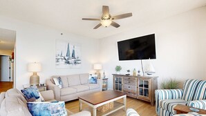 Ein Wohnzimmer mit Sofa, Sesseln, Couchtisch, Fernseher und Deckenventilator.