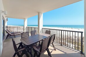Un balcón con mesa y sillas, vista a la playa y barandilla.