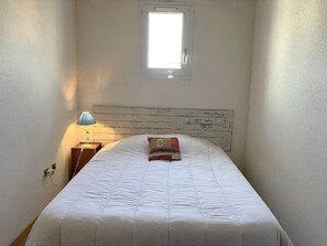 A bedroom with a bed, a nightstand, a lamp, a window, and a wooden headboard. - Goutte d'eau - Saint Hilaire de riez (SAINT HILAIRE DE RIEZ)