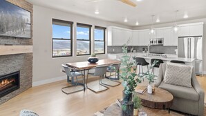 A modern living room with a fireplace, a dining area, and a kitchen with white cabinets and stainless steel appliances. - Mayflower Lakeside 104 | Reservoir + Mountain View | Full Kitchen | Private Bedrooms (Heber City)