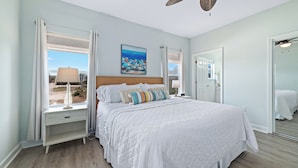 A bedroom with a large bed, a nightstand, a window with curtains, a ceiling fan, and a painting on the wall. - Spacious 4BR beach house with Hot Tub/Fire Pit /Ping Pong/Foosball/Beach gear (Orange Beach)