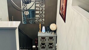 Un escalier orné d’un lustre, un miroir décoratif, un globe terrestre et une petite armoire.