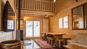 Interior de uma cabana de madeira com lareira, mesa de jantar e sofá.