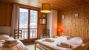 Um quarto de madeira aconchegante com duas camas, uma janela com vista para montanhas cobertas de neve e teto de madeira.