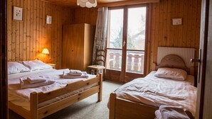 Quarto de madeira com duas camas, uma luminária e vista para árvores pela janela.