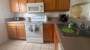 A compact kitchen with wooden cabinets, a microwave, a stove, and a sink. - Home in Kissimmee near Disney and Universal (Kissimmee)