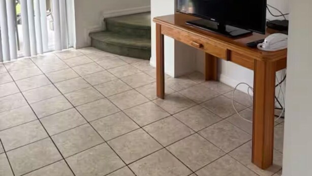 A spacious room with a tiled floor, a wooden table with a television, and a set of stairs leading to another area. - Home in Kissimmee near Disney and Universal (Kissimmee)
