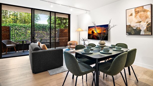 Un comedor moderno con una mesa preparada para cuatro personas, un sofá y vistas a un jardín a través de grandes ventanales.