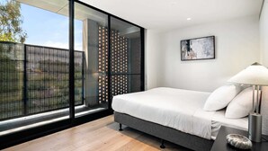 Un dormitorio moderno con un ventanal grande, una cama, una mesita de noche y una lámpara.