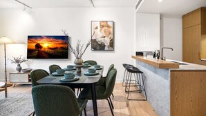 Un comedor moderno con una mesa preparada para cuatro, una cocina con encimera de madera y dos cuadros en la pared.