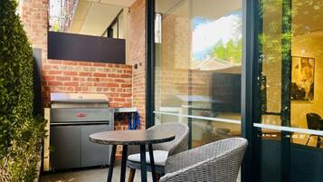 A patio area with a grill, wicker chairs, and a glass wall offering a view of the outdoors.