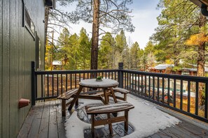En træterrasse med et bord og bænke, omgivet af gelænder, med udsigt over et skovområde.