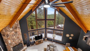Una sala de estar acogedora con chimenea de piedra, ventanas amplias y un ventilador de techo.