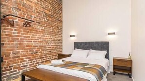 Ein Schlafzimmer mit Backsteinwand, einem Bett mit weißer Bettwäsche, einer Holzbank und zwei Nachttischen.