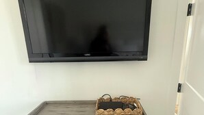 Un televisor montado en la pared sobre una consola de madera con una cesta tejida y un protector contra sobretensiones.