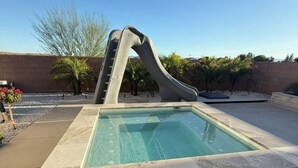 Una piscina con tobogán, rodeada por un muro de ladrillo y palmeras.