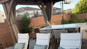 Dos sillones con cojines blancos y detalles azules, ubicados en un patio con una mesa y sillas al fondo.