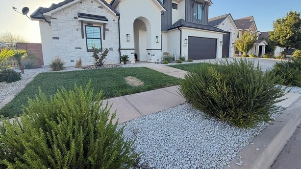 Una casa moderna de dos pisos con fachada de piedra, garaje y césped cuidado con arbustos y senderos de grava.