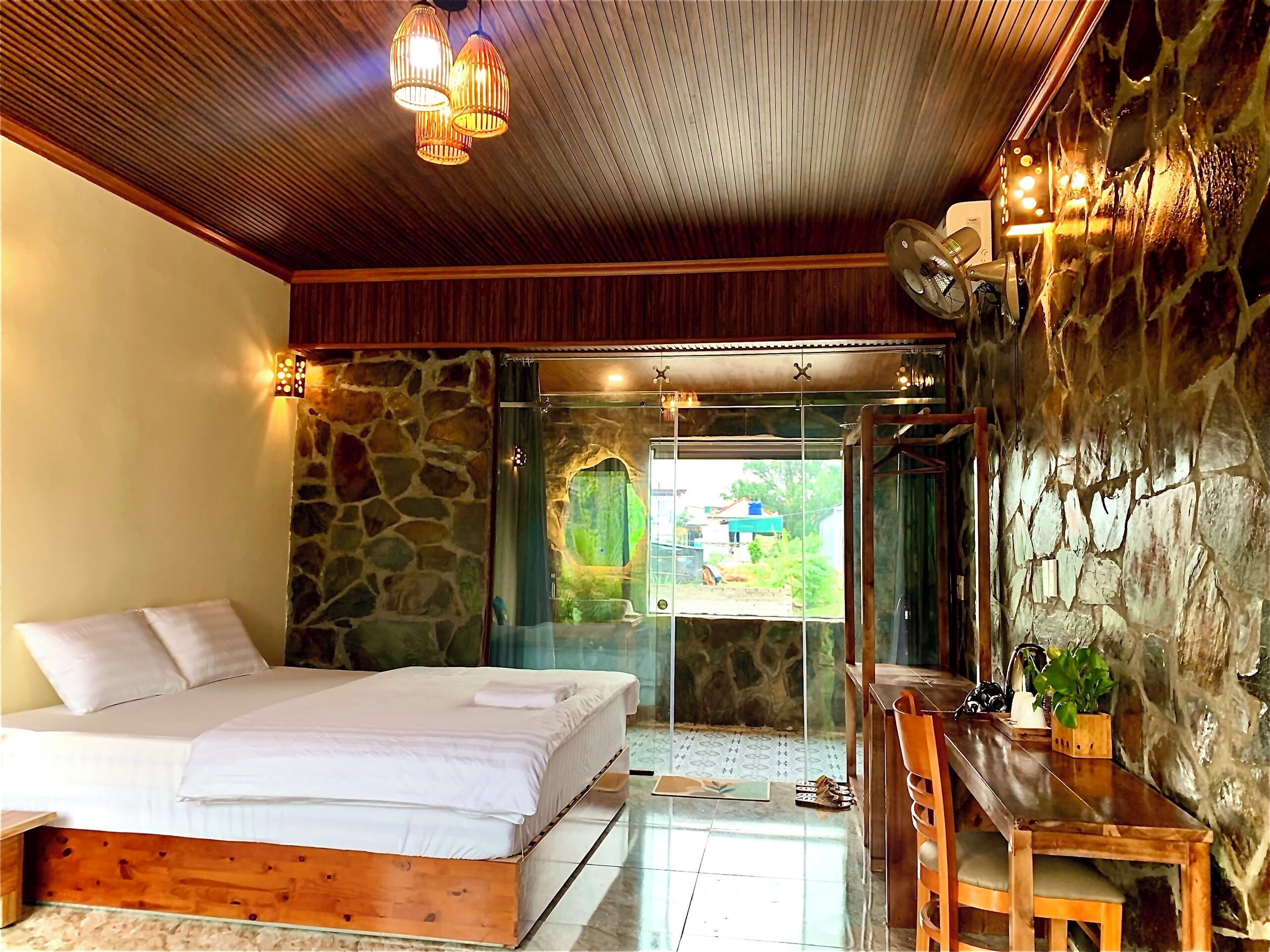 A bedroom with a bed, a desk, and a stone wall.