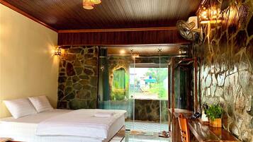 A bedroom with a bed, a desk, and a stone wall.