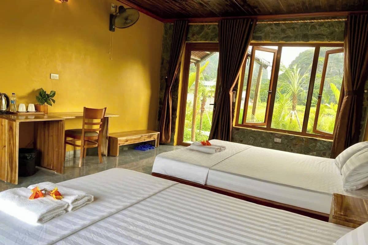 Habitación de hotel con dos camas, un escritorio y una silla. Cuenta con un ventanal con cortinas y vistas al exterior.