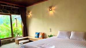 A bedroom with a large bed, a bench, a window with curtains, and a wall-mounted light fixture. - Rocky Mountain Ecolodge (Ninh Binh)