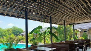 An outdoor seating area with wooden benches and tables, overlooking a swimming pool and lush greenery. - Rocky Mountain Ecolodge (Ninh Binh)