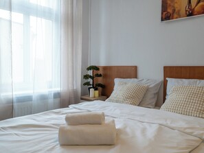 A neatly made bed with white linens and two towels, a bedside table with a small potted plant, and a painting on the wall. - Zabrze City Comfort Room 1 (Zabrze)