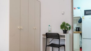 A compact room with a wardrobe, a desk with a chair, a potted plant, a bottle, and a microwave. - Zabrze City Comfort Room 1 (Zabrze)