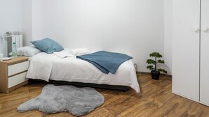 Ein Schlafzimmer mit einem Bett, einem Nachttisch, einer Wasserflasche, einer Topfpflanze und einem grauen Fellteppich.
